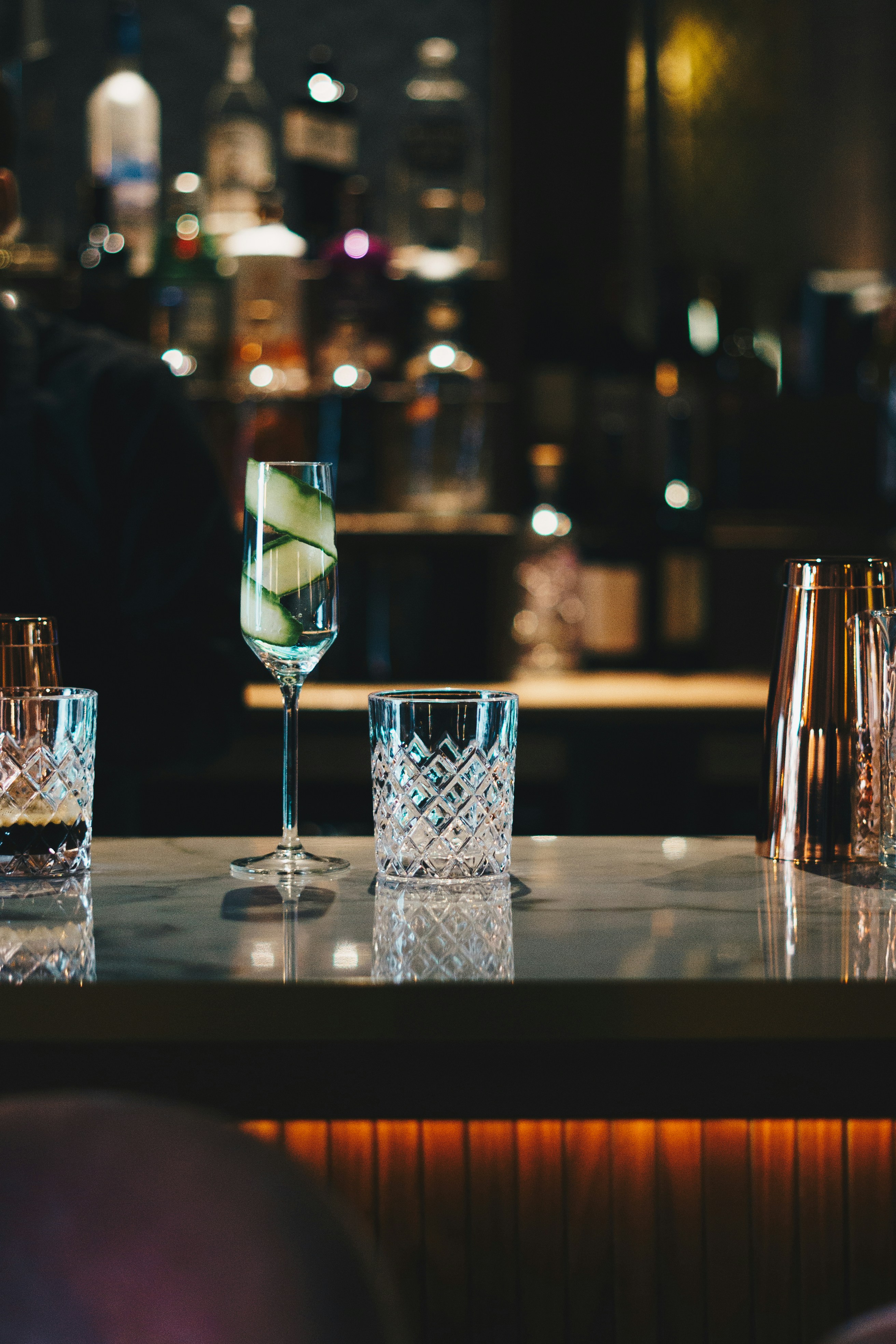 Crystal glassware on a marble bar top at SIP/STER, with softly lit bottles behind.